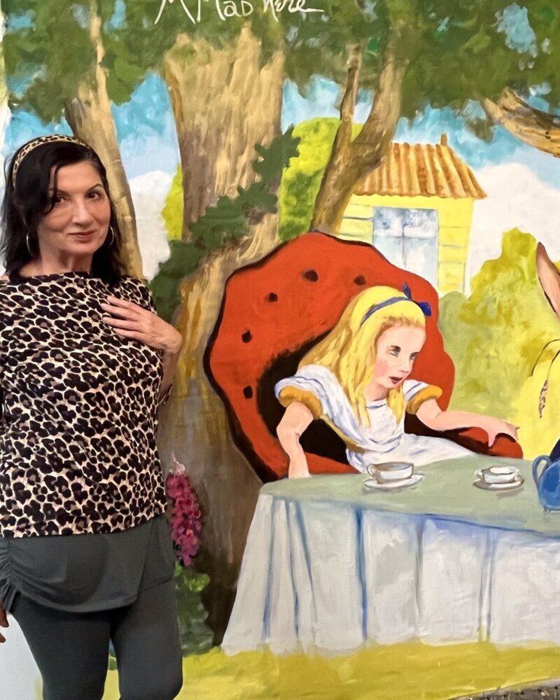 Maureen Fulgenzi beside a completed Alice in Wonderland mural