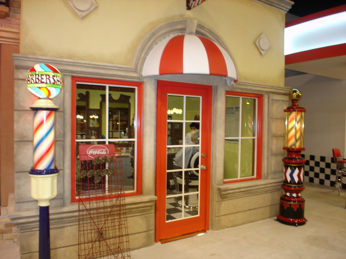 Barber shop storefront mural with red-and-white barber pole, car museum backdrop, Palm Beach, FL