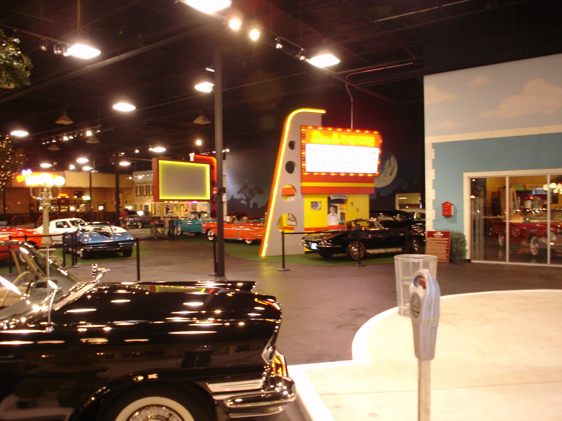 Wide night view of the museum showroom floor with painted streetscape mural and classic cars, Palm Beach, FL