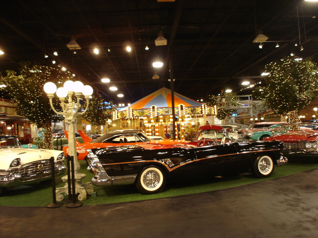 Wide interior view of the car museum showroom with classic cars beneath the painted streetscape mural, Palm Beach, FL