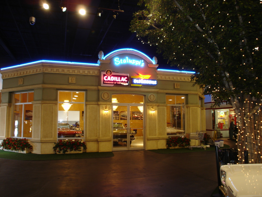 Night exterior mural view of a diner storefront with neon signage, car museum backdrop, Palm Beach, FL
