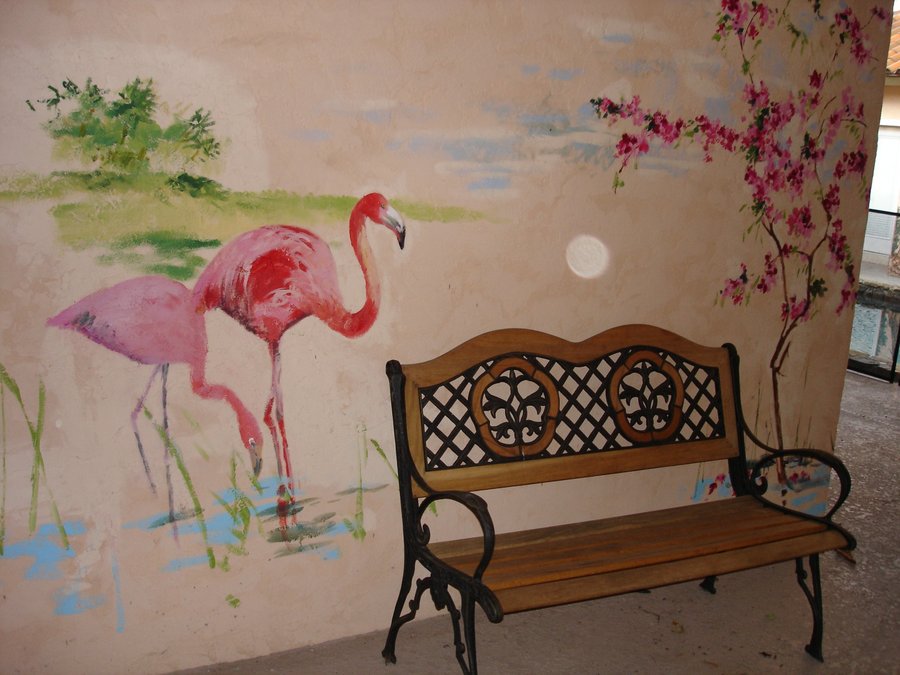 Painted flamingos wading in reeds, exterior wall mural beside a garden bench, Palm Beach, FL