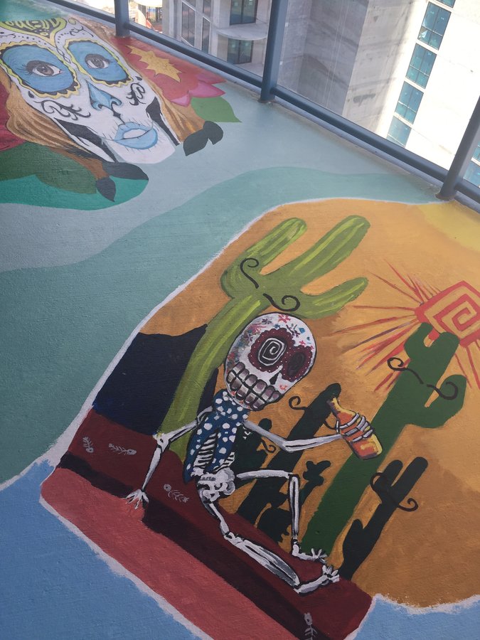 Skeleton figure in a polka-dot shawl toasting with a bottle, cactus backdrop, exterior terrace mural, Palm Beach, FL