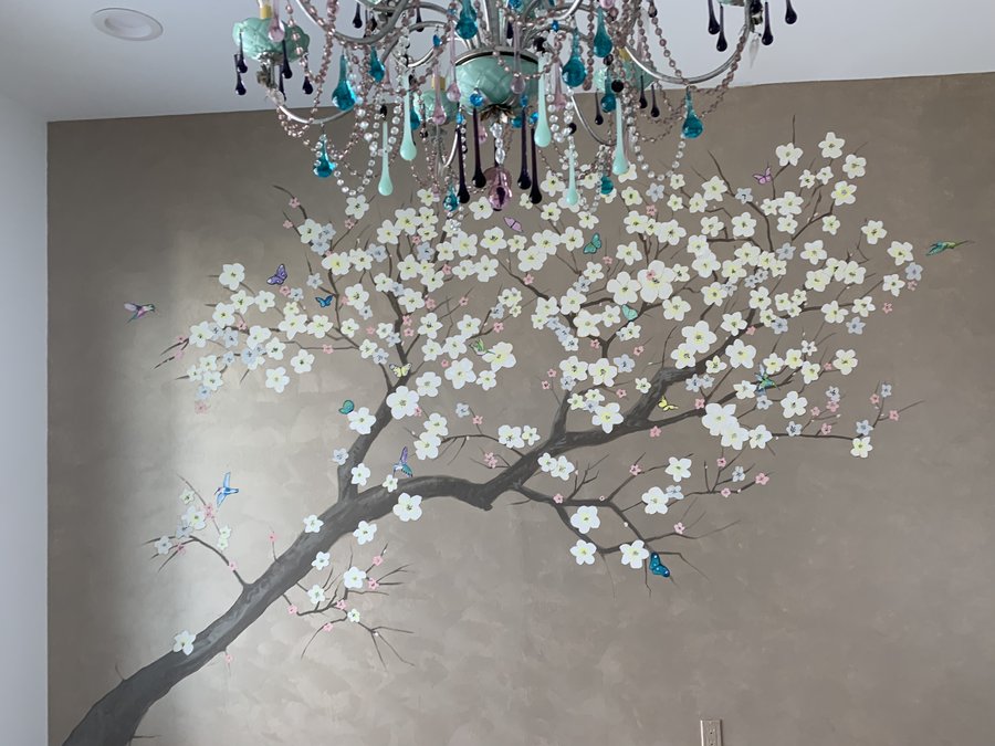 White blossom branch mural with hummingbirds and butterflies beneath a crystal chandelier, gold metallic wall, Palm Beach, FL
