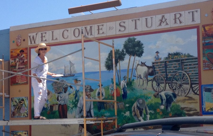 Maureen Fulgenzi painting the Stuart mural from scaffolding, early stage, blue sky visible, Palm Beach, FL