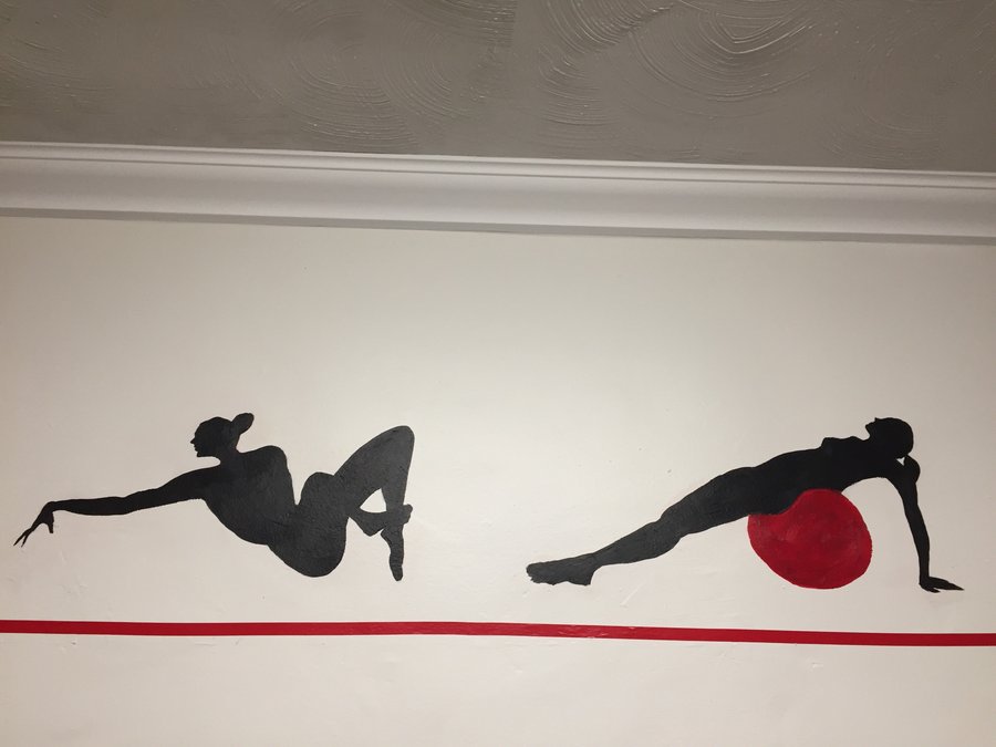 Arm-raise and stability-ball silhouette figures painted along the gym mural border, Palm Beach, FL