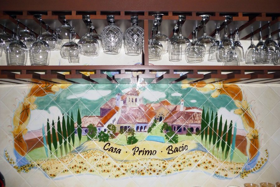 Small painted tile mosaic sign reading Casa Primo Bacio, below the wine rack, restaurant wall, Palm Beach, FL