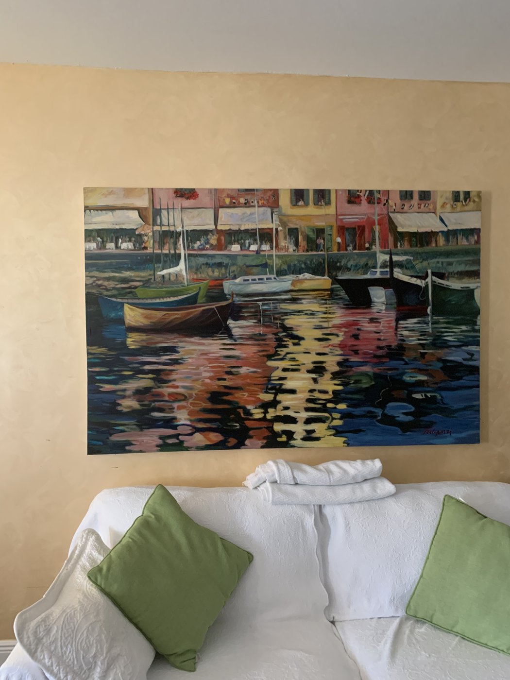 Harbor and sailboat painting by Maureen Fulgenzi above a sofa with green pillows in a neutral living room, Palm Beach, FL
